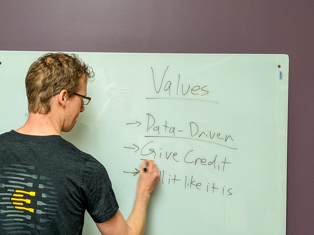 Stuart Diller writing the company values on a whiteboard. The board reads: data-driven, give credit, call it like it is